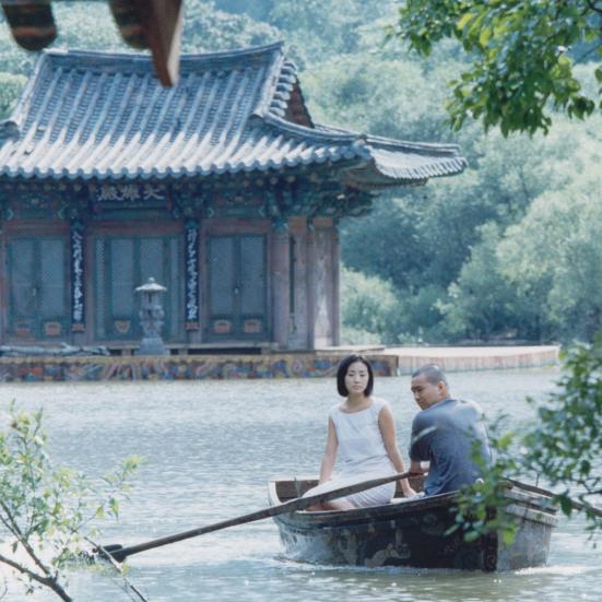 Mand og kvinde i en båd på en sø, foran et koreansk hus.